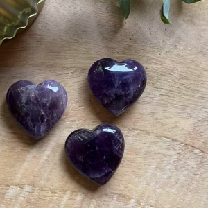 Amethist Hartje op houten tafel met kaars, Amethist Hart met zijn diep paarse kleur en glinstering, Amethist die gebruikt kan worden bij edelsteentherapie en de werking van edelstenen