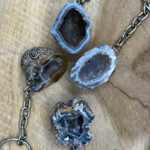 Unieke Agaat Geode Sleutelhanger met kristallen binnenkant, Agaat Hanger met natuurlijke geode structuur op houten ondergrond, Hand met Agaat Geode Sleutelhanger tegen zonlicht