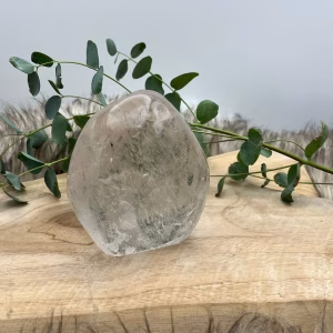 Bergkristal Freeform op houten tafel met zonlicht, Uniek gevormde bergkristal Freeform naast meditatiekaars, Bergkristal reinigen en opladen onder maanlicht