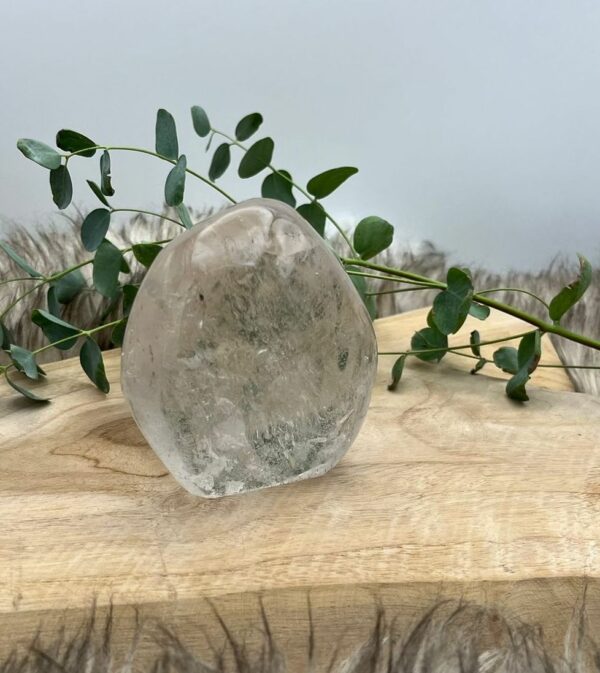 Bergkristal Freeform op houten tafel met zonlicht, Uniek gevormde bergkristal Freeform naast meditatiekaars, Bergkristal reinigen en opladen onder maanlicht
