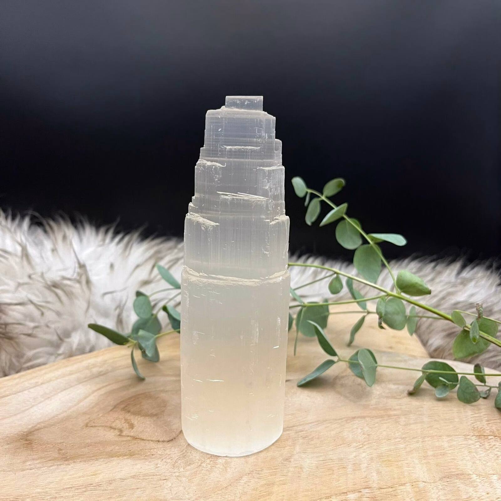 Seleniet toren 15 cm op een houten tafel met kaarsen en edelstenen, Glanzende seleniet toren in een spirituele meditatiehoek, Seleniet toren naast andere mineralen voor energiezuivering, Seleniet toren, Seleniet toren 15 cm
