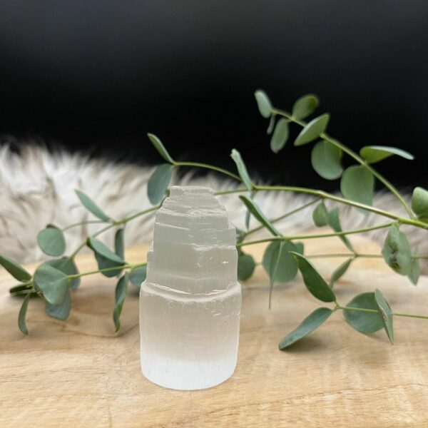 Seleniet toren 6 cm op een houten tafel met kaarsen en edelstenen, Glanzende seleniet toren in een spirituele meditatiehoek, Seleniet toren naast andere mineralen voor energiezuivering, Seleniet toren, Seleniet toren 6 cm