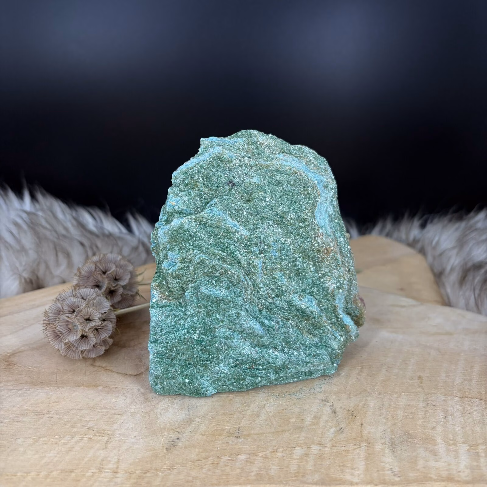 Fuchsiet Cut-Base van 11 cm hoog met een sprankelende groene glans, Detail van de mica schittering in een Fuchsiet van 603 gram, Zijaanzicht van de 4 cm diepe Fuchsiet op een vlakke voet, Groene Fuchsiet Cut-Base op een houten plank in een lichte kamer.