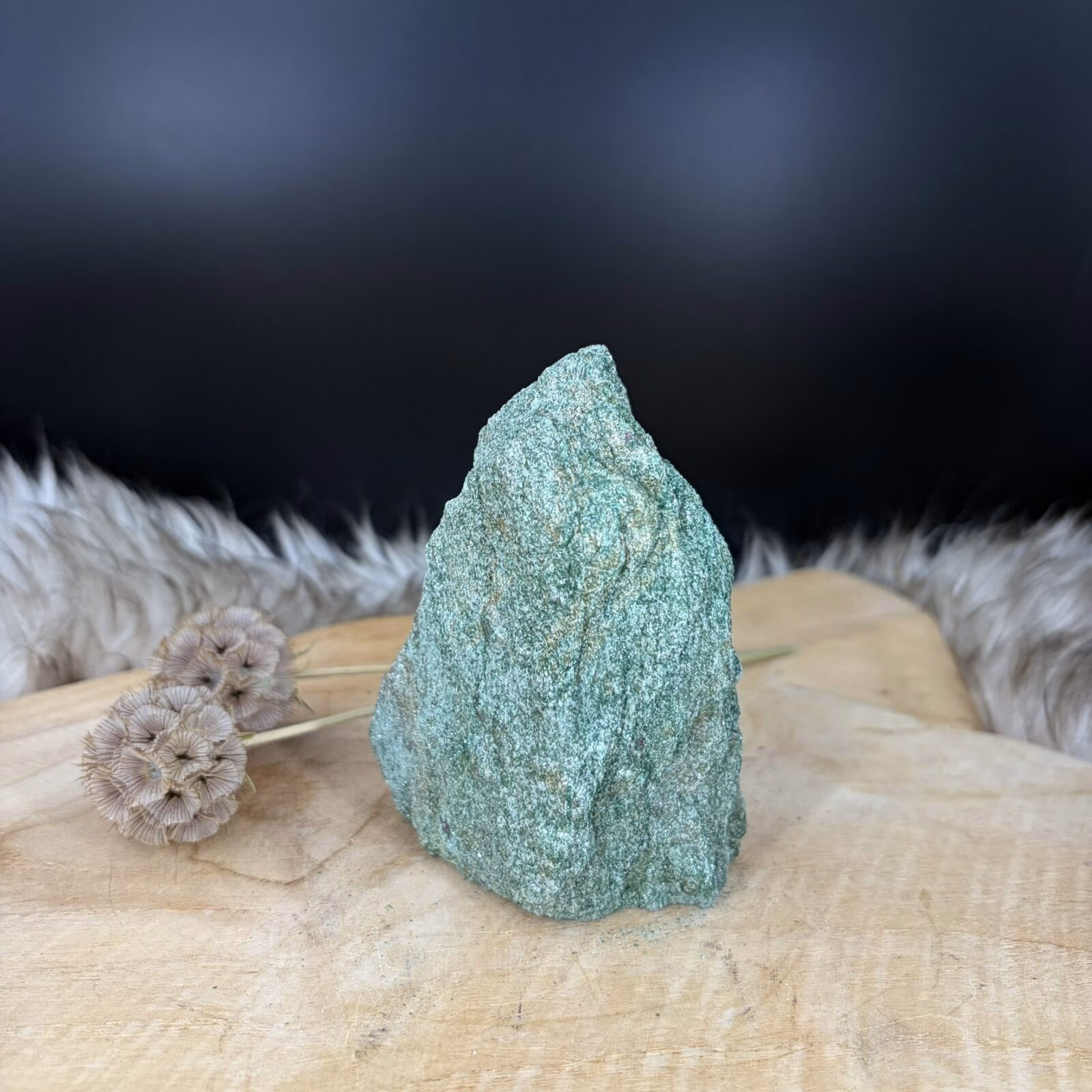 Fuchsiet Freeform van 10 cm hoog met een sprankelende groene kleur, Detail van de glinstering in een Fuchsiet van 506 gram, Zijaanzicht van de 5 cm diepe Freeform Fuchsiet met mica schittering, Groene Fuchsiet op een houten ondergrond in een sfeervol interieur.