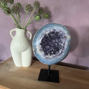 Amethist Geode op standaard, Een glanzende Amethist Geode op zwarte standaard, close-up van de kristallen in de Amethist Geode, zijkant van een grote Amethist Geode met diepe paarse punten, sfeervolle woonkamer met Amethist Geode als decoratie, detailfoto van glinsterende amethistkristallen, Amethist Geode op standaard bij een meditatiehoek, natuurlijk gevormde Amethist Geode met unieke structuur, Amethist Geode op standaard met zachte verlichting eromheen, overzicht van verschillende Amethist Geodes op standaard in een interieursetting.