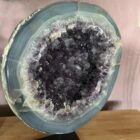 Amethist Geode op standaard, Een glanzende Amethist Geode op zwarte standaard, close-up van de kristallen in de Amethist Geode, zijkant van een grote Amethist Geode met diepe paarse punten, sfeervolle woonkamer met Amethist Geode als decoratie, detailfoto van glinsterende amethistkristallen, Amethist Geode op standaard bij een meditatiehoek, natuurlijk gevormde Amethist Geode met unieke structuur, Amethist Geode op standaard met zachte verlichting eromheen, overzicht van verschillende Amethist Geodes op standaard in een interieursetting.