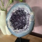 Amethist Geode op standaard, Een glanzende Amethist Geode op zwarte standaard, close-up van de kristallen in de Amethist Geode, zijkant van een grote Amethist Geode met diepe paarse punten, sfeervolle woonkamer met Amethist Geode als decoratie, detailfoto van glinsterende amethistkristallen, Amethist Geode op standaard bij een meditatiehoek, natuurlijk gevormde Amethist Geode met unieke structuur, Amethist Geode op standaard met zachte verlichting eromheen, overzicht van verschillende Amethist Geodes op standaard in een interieursetting.