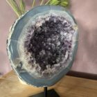Amethist Geode op standaard, Een glanzende Amethist Geode op zwarte standaard, close-up van de kristallen in de Amethist Geode, zijkant van een grote Amethist Geode met diepe paarse punten, sfeervolle woonkamer met Amethist Geode als decoratie, detailfoto van glinsterende amethistkristallen, Amethist Geode op standaard bij een meditatiehoek, natuurlijk gevormde Amethist Geode met unieke structuur, Amethist Geode op standaard met zachte verlichting eromheen, overzicht van verschillende Amethist Geodes op standaard in een interieursetting.