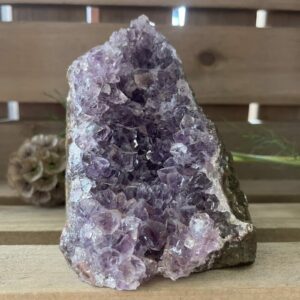 amethist cut base op houten tafel met kaarsen, ruwe amethist steen met paarse glans in daglicht, spirituele amethist decoratie bij meditatieplek, close-up van amethist kristal met diepe insnijdingen, energetische amethist steen naast reinigingsritueel
