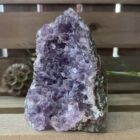 amethist cut base op houten tafel met kaarsen, ruwe amethist steen met paarse glans in daglicht, spirituele amethist decoratie bij meditatieplek, close-up van amethist kristal met diepe insnijdingen, energetische amethist steen naast reinigingsritueel