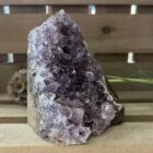 amethist cut base op houten tafel met kaarsen, ruwe amethist steen met paarse glans in daglicht, spirituele amethist decoratie bij meditatieplek, close-up van amethist kristal met diepe insnijdingen, energetische amethist steen naast reinigingsritueel