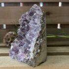 amethist cut base op houten tafel met kaarsen, ruwe amethist steen met paarse glans in daglicht, spirituele amethist decoratie bij meditatieplek, close-up van amethist kristal met diepe insnijdingen, energetische amethist steen naast reinigingsritueel