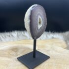 Agaat geode op zwart metalen voetstuk met glanzende kristallen, Detail van sprankelende kristalstructuur binnenin de agaat, Zijaanzicht van kleine agaat geode met natuurlijke patronen, Agaat geode in spirituele setting met kaars en veer, Close-up van geode-opening met fijne kristallen en aardse kleuren