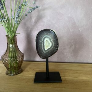 Agaat geode op zwart metalen voetstuk met glanzende kristallen, Detail van sprankelende kristalstructuur binnenin de agaat, Zijaanzicht van kleine agaat geode met natuurlijke patronen, Agaat geode in spirituele setting met kaars en veer, Close-up van geode-opening met fijne kristallen en aardse kleuren