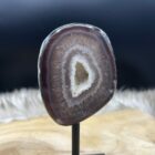 Agaat geode op zwart metalen voetstuk met glanzende kristallen, Detail van sprankelende kristalstructuur binnenin de agaat, Zijaanzicht van kleine agaat geode met natuurlijke patronen, Agaat geode in spirituele setting met kaars en veer, Close-up van geode-opening met fijne kristallen en aardse kleuren