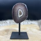 Agaat geode op zwart metalen voetstuk met glanzende kristallen, Detail van sprankelende kristalstructuur binnenin de agaat, Zijaanzicht van kleine agaat geode met natuurlijke patronen, Agaat geode in spirituele setting met kaars en veer, Close-up van geode-opening met fijne kristallen en aardse kleuren