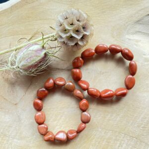 Rode jaspis freeform armband op houten ondergrond met zonlicht, Pols met freeform armband van rode jaspis kralen, Close-up van ruwe rode jaspis kralen in natuurlijke vorm, Spirituele setting met rode jaspis armband en kaarsen, Rode jaspis armband 4 mm gedragen bij altaarsteen