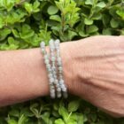 Labradoriet armband 4 mm met iriserende glans, Close-up van labradoriet kralen met blauwe en gouden schakeringen, Labradoriet armband gedragen om de pols in natuurlijk licht, Stapel armbanden met labradoriet als beschermende steen, Labradoriet armband 4 mm in spirituele setting met salie en kristallen