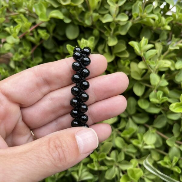 Zwarte agaat armband met dubbele rij kralen en treksluiting op houten ondergrond, Detail van verstelbare zwarte agaat armband met 6 mm kralen, Pols met dubbele zwarte agaat armband tijdens meditatie, Spirituele setting met zwarte agaat armband op altaar, Zwarte agaat armband gecombineerd met hematiet en rookkwarts