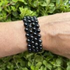 Zwarte agaat armband met dubbele rij kralen en treksluiting op houten ondergrond, Detail van verstelbare zwarte agaat armband met 6 mm kralen, Pols met dubbele zwarte agaat armband tijdens meditatie, Spirituele setting met zwarte agaat armband op altaar, Zwarte agaat armband gecombineerd met hematiet en rookkwarts