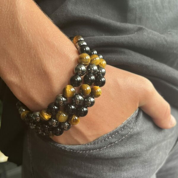 Armband van hematiet, obsidiaan en tijgeroog op houten altaar, Detail van 8 mm kralen in aardende kleurcombinatie, Pols met krachtige drievoudige edelsteenarmband, Spirituele setting met hematiet-obsidiaan-tijgeroog armband, Armband naast palo santo en seleniet bij volle maanritueel