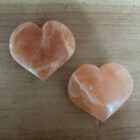 oranje seleniet hart met warme gloed op houten tafel, close-up van oranje kristal in hartvorm met zachte randen, spiritueel altaar met seleniet hart en kaarslicht, 7 cm oranje seleniet op vensterbank in zonsondergang, hand houdt hartvormige oranje steen tegen rustige achtergrond