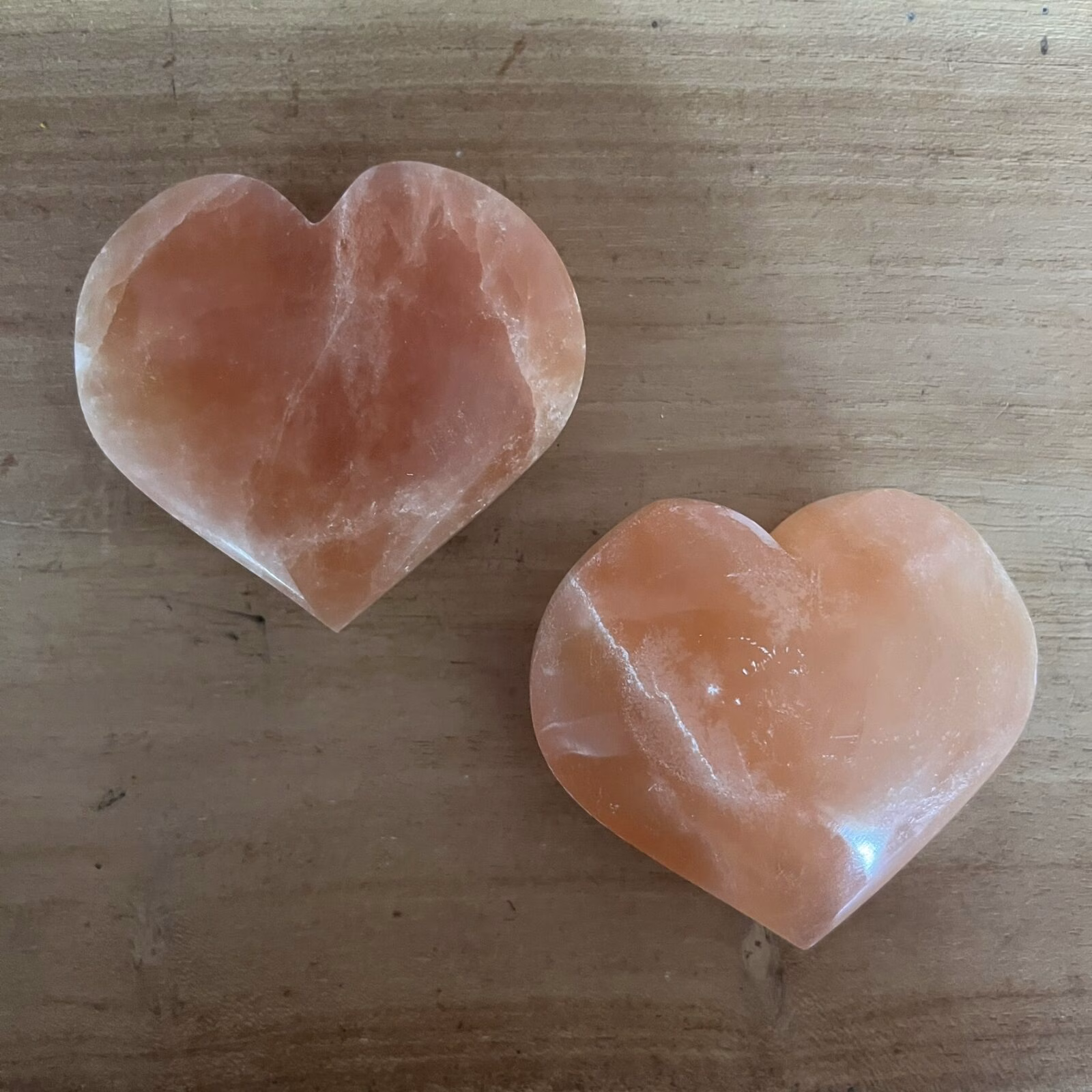 oranje seleniet hart met warme gloed op houten tafel, close-up van oranje kristal in hartvorm met zachte randen, spiritueel altaar met seleniet hart en kaarslicht, 7 cm oranje seleniet op vensterbank in zonsondergang, hand houdt hartvormige oranje steen tegen rustige achtergrond