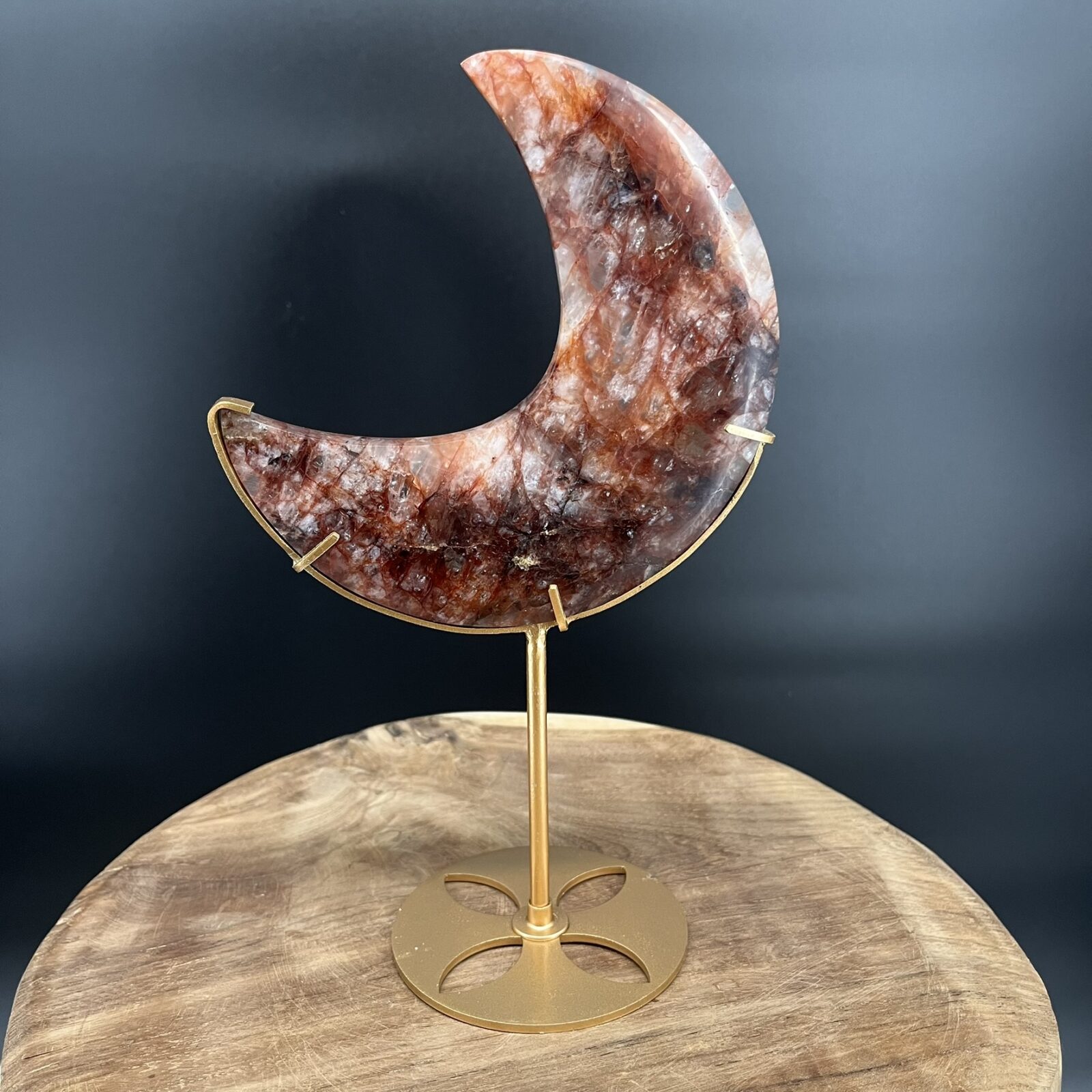 Fire Quartz Moon op Standaard 514 gram, vuurkwarts maan met rode hematietaders, Fire Quartz Moon op houten tafel bij kaarslicht, detail van hematoïde kwarts in Fire Quartz Moon, Fire Quartz Moon op goudkleurige standaard in woonkamer, Fire Quartz Moon als spirituele decoratie bij altaar.
