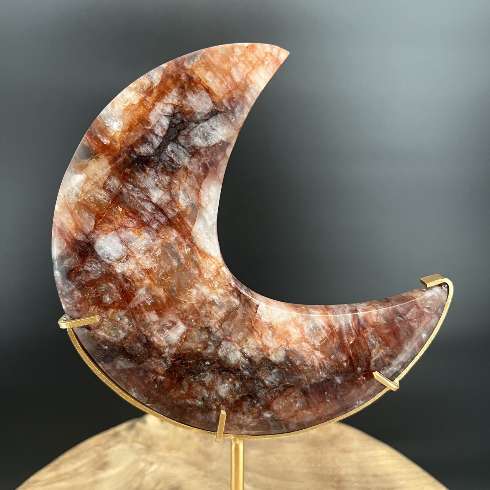 hematoïde kwarts op standaard, fire quartz op standaard, Fire Quartz Moon op Standaard 514 gram, vuurkwarts maan met rode hematietaders, Fire Quartz Moon op houten tafel bij kaarslicht, detail van hematoïde kwarts in Fire Quartz Moon, Fire Quartz Moon op goudkleurige standaard in woonkamer, Fire Quartz Moon als spirituele decoratie bij altaar.
