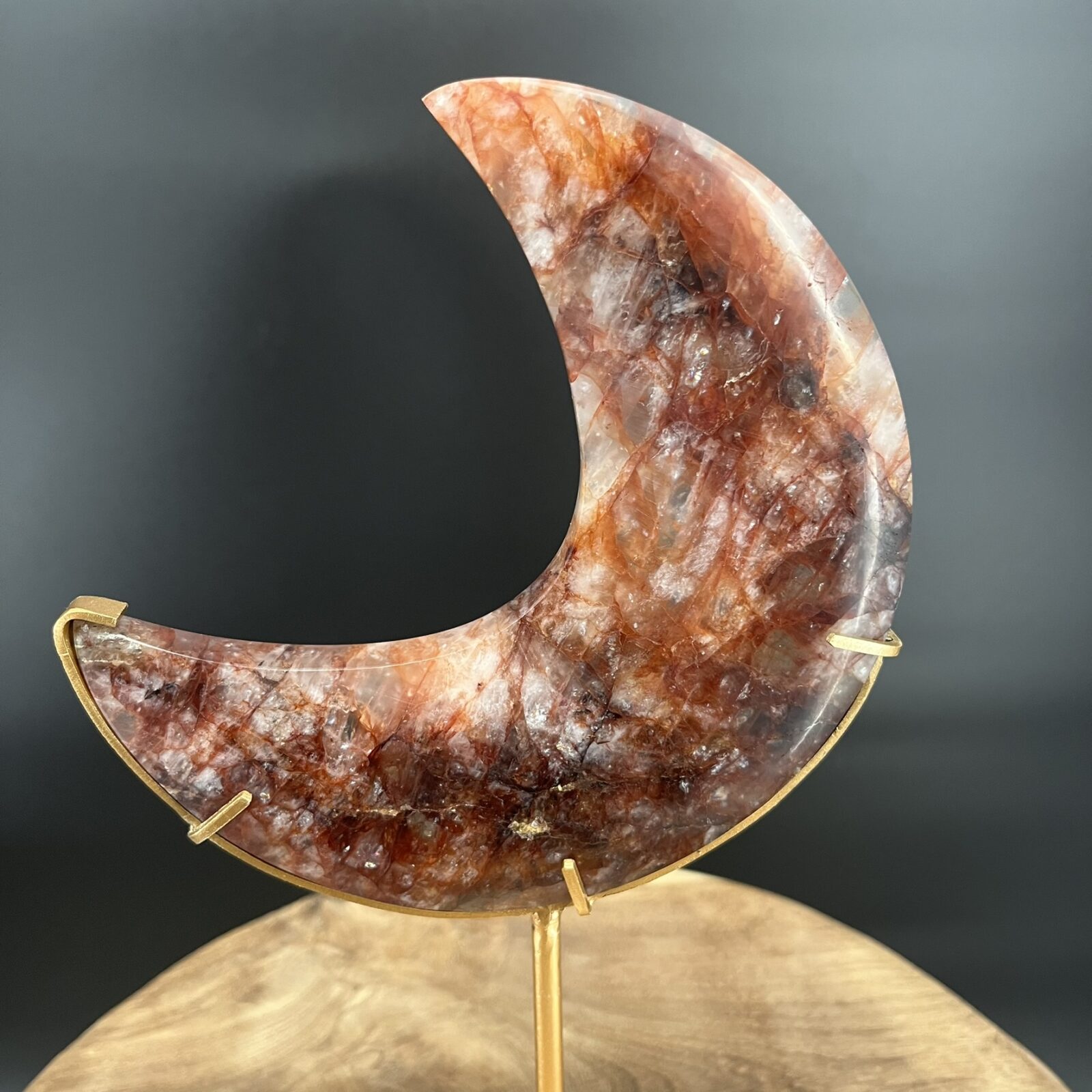 Fire Quartz Moon op Standaard 514 gram, vuurkwarts maan met rode hematietaders, Fire Quartz Moon op houten tafel bij kaarslicht, detail van hematoïde kwarts in Fire Quartz Moon, Fire Quartz Moon op goudkleurige standaard in woonkamer, Fire Quartz Moon als spirituele decoratie bij altaar.