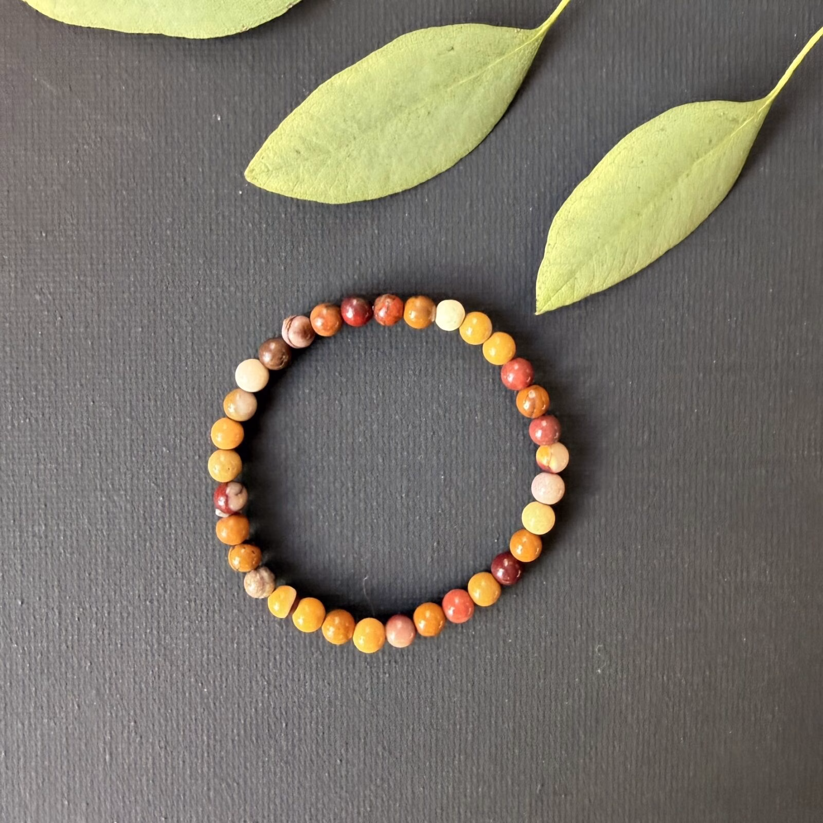 Mookaiet jaspis kinderarmband met 4 mm kralen in warme herfstkleuren zoals geel en rood, detailopname van de kleurrijke mookaiet jaspis kralen van een elastisch kinderarmbandje, mookaiet jaspis kinderarmband gedragen om een kleine pols voor extra moed en energie, kleurrijke edelsteen armband van mookaiet jaspis speciaal voor kinderen, mookaiet jaspis kinderarmband liggend op een lichte ondergrond die de natuurlijke variatie van de stenen toont, handgemaakte kinderarmband met mookaiet jaspis kralen voor een vrolijke en beschermende uitstraling.