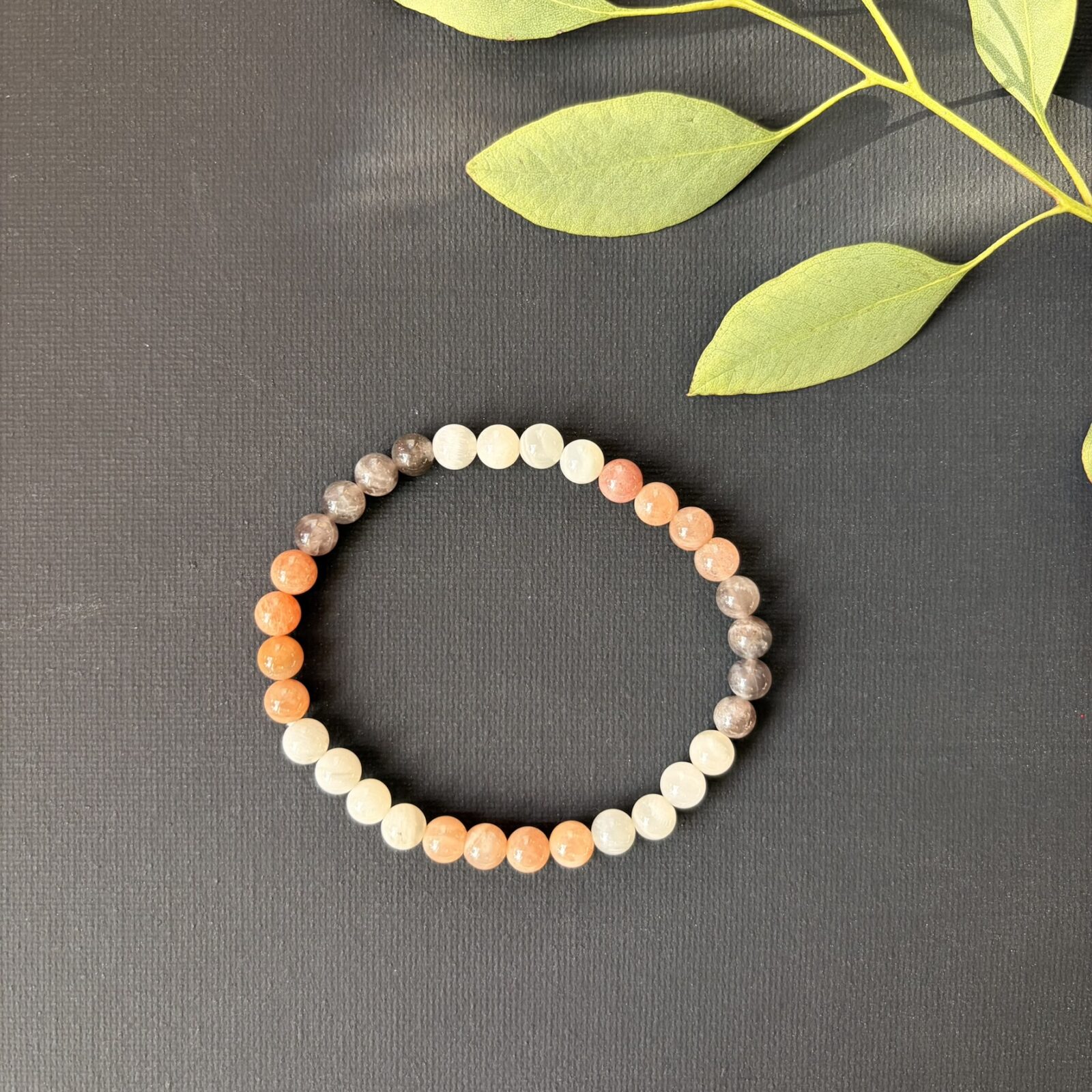 'Maansteen mix armband 6 mm, Gepolijste maansteen mix armband met 6 mm kralen in zachte tinten grijs en wit, close-up van een elastische maansteen armband met natuurlijke kleurnuances van crème tot zilver, maansteen mix armband 6 mm gedragen om een pols voor een rustige uitstraling, collectie maansteen armbanden met 6 mm kralen die de natuurlijke glans van de steen tonen, maansteen mix armband 6 mm liggend op een houten ondergrond voor een natuurlijke sfeer, detailopname van de gladde 6 mm kralen van een maansteen mix armband bij daglicht, maansteen mix armband 6 mm naast een op- en ontlaadsetje van Natuursteentje, handgemaakte maansteen armband met kralen van 6 mm die de zachte energie van de maansteen weerspiegelen.