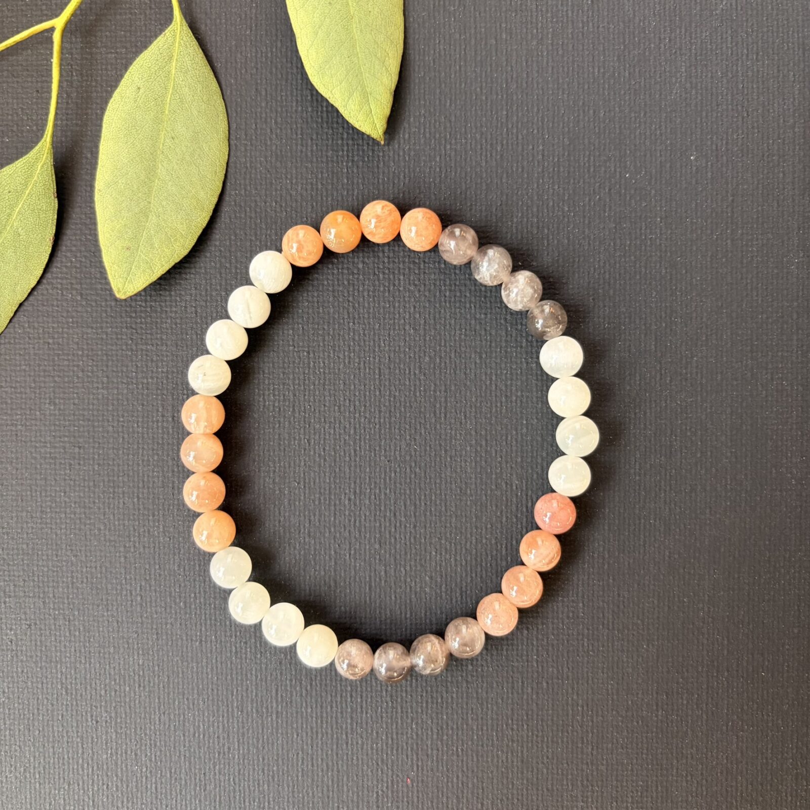 'Maansteen mix armband 6 mm, Gepolijste maansteen mix armband met 6 mm kralen in zachte tinten grijs en wit, close-up van een elastische maansteen armband met natuurlijke kleurnuances van crème tot zilver, maansteen mix armband 6 mm gedragen om een pols voor een rustige uitstraling, collectie maansteen armbanden met 6 mm kralen die de natuurlijke glans van de steen tonen, maansteen mix armband 6 mm liggend op een houten ondergrond voor een natuurlijke sfeer, detailopname van de gladde 6 mm kralen van een maansteen mix armband bij daglicht, maansteen mix armband 6 mm naast een op- en ontlaadsetje van Natuursteentje, handgemaakte maansteen armband met kralen van 6 mm die de zachte energie van de maansteen weerspiegelen.