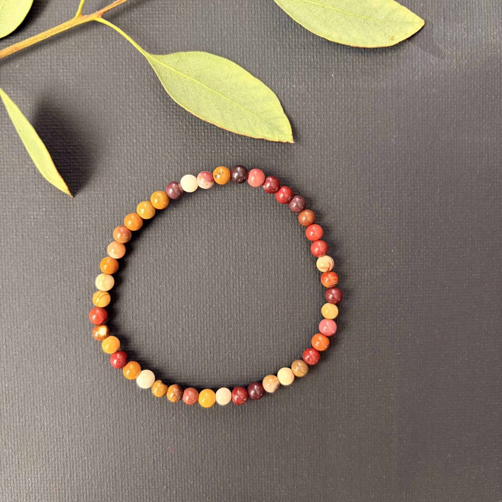 Subtiele Mookaiet Jaspis armband met kleine 4 mm kralen in vrolijke geel- en roodtinten, detailopname van een elastische armband met verfijnde mookaiet jaspis kralen van hoge kwaliteit, Mookaiet Jaspis armband 4 mm gedragen om de pols voor een elegante en kleurrijke uitstraling, verfijnde edelsteen armband van mookaiet jaspis met 4 mm kralen voor nieuwe energie, Mookaiet Jaspis armband 4 mm liggend op een lichte ondergrond die de natuurlijke patronen toont, handgemaakte armband met kleine mookaiet jaspis kralen van 4 mm die levenslust en rust uitstralen.