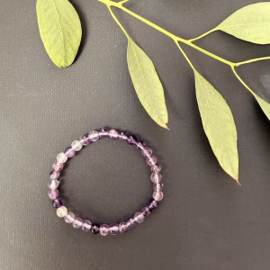 Paarse Fluoriet kinderarmband, Paarse fluoriet kinderarmband met kleine kralen in zachte en diepe paarse tinten, detailopname van een elastisch kinderarmbandje met natuurlijke paarse fluoriet kralen, paarse fluoriet kinderarmband gedragen om een kleine pols voor betere focus en concentratie, kleurrijke edelsteen armband van paarse fluoriet speciaal voor kinderen, paarse fluoriet kinderarmband liggend op een lichte ondergrond die de transparante glans toont, handgemaakte kinderarmband met paarse fluoriet kralen die rust en mentale helderheid uitstralen.