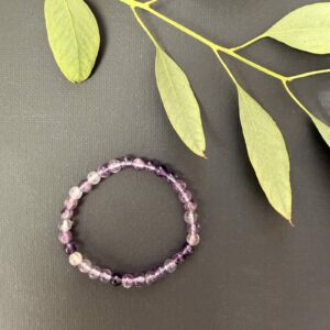 Paarse Fluoriet kinderarmband, Paarse fluoriet kinderarmband met kleine kralen in zachte en diepe paarse tinten, detailopname van een elastisch kinderarmbandje met natuurlijke paarse fluoriet kralen, paarse fluoriet kinderarmband gedragen om een kleine pols voor betere focus en concentratie, kleurrijke edelsteen armband van paarse fluoriet speciaal voor kinderen, paarse fluoriet kinderarmband liggend op een lichte ondergrond die de transparante glans toont, handgemaakte kinderarmband met paarse fluoriet kralen die rust en mentale helderheid uitstralen.