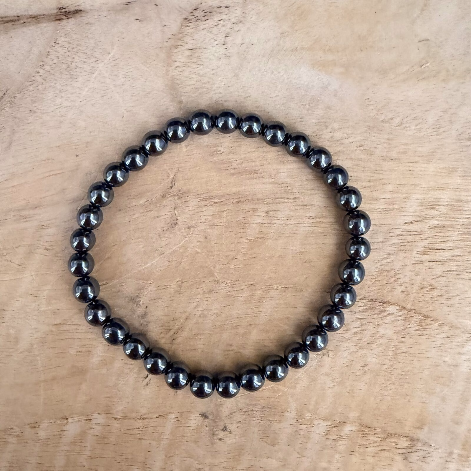 Hematiet armband 6 mm, Hematiet armband, Hematiet armband met metallic grijze kralen van 6 mm voor dagelijkse aarding, edelsteen armband van 6 mm hematiet kralen voor extra zelfvertrouwen en rust, close-up van een glanzende grijze hematiet armband van hoge kwaliteit, handgemaakte armband met 6 mm hematiet kristallen tegen negatieve energie, spirituele hematiet armband met 6 mm kralen die beschermt tegen prikkels van buitenaf, detailfoto van een hematiet 6 mm armband met een stoere spiegelende glans.