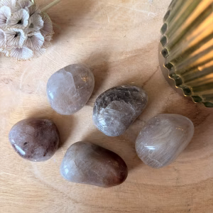 Rutielkwarts, Rutielkwarts Trommelsteen in een groepje van vijf, Rutielkwarts bij kaarslicht, Rutielkwarts trommelsteen 20 gram voor spirituele groei en hoop, heldere edelsteen met gouden rutielnaaldjes bij Natuursteentje, handgeselecteerde Rutielkwarts kopen voor focus, spirituele werking Rutielkwarts tegen angsten, edelsteen combinatie met Citrien en Rookkwarts, unieke trommelsteen webshop Natuursteentje.