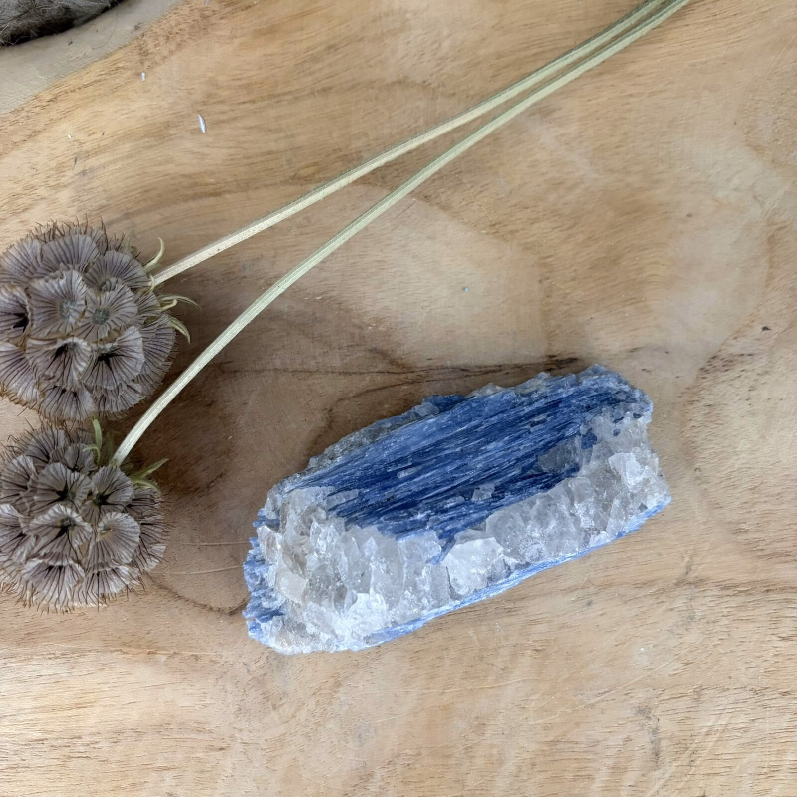 Blauwe Kyaniet van 9 cm lang met een glanzende gelaagde structuur, Detail van de diepblauwe banen in een Kyaniet van 119 gram, Kyaniet mineraal met een trikliene kristalvorm op een lichte achtergrond, Blauwe Kyaniet op een houten tafel voor rust en communicatie in huis.
