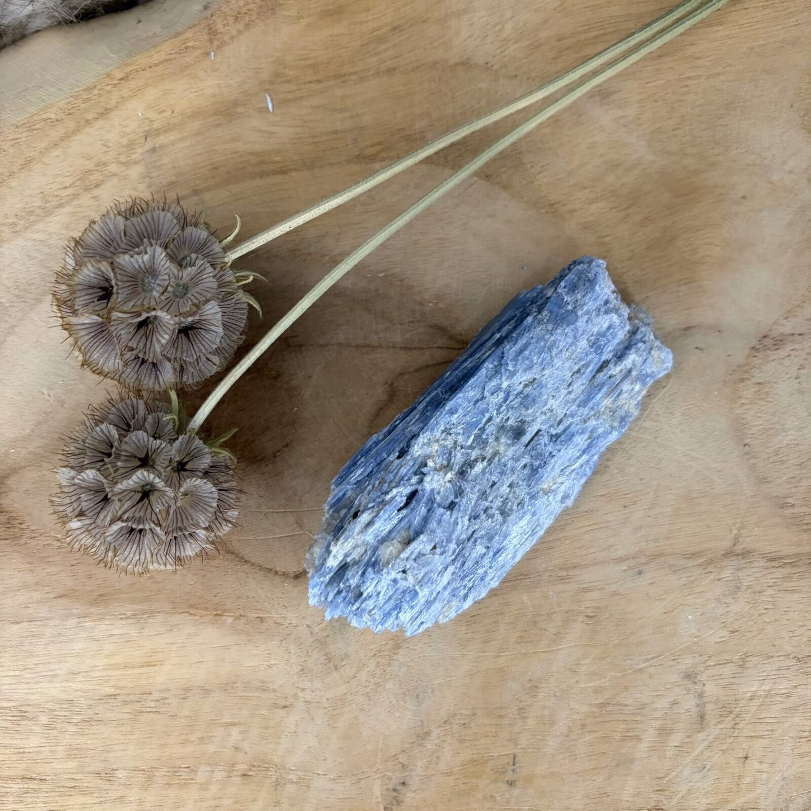 Blauwe Kyaniet van 9 cm lang met een glanzende gelaagde structuur, Detail van de diepblauwe banen in een Kyaniet van 119 gram, Kyaniet mineraal met een trikliene kristalvorm op een lichte achtergrond, Blauwe Kyaniet op een houten tafel voor rust en communicatie in huis.