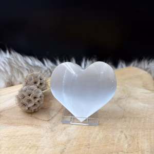 Wit Seleniet Hart met satijnachtige glans van 7 cm breed, Handgeslepen hart van wit seleniet uit Marokko voor meditatie, Detail van de glanzende vezelige structuur in een wit seleniet hart, Seleniet hart op een nachtkastje voor een rustige sfeer in de slaapkamer.