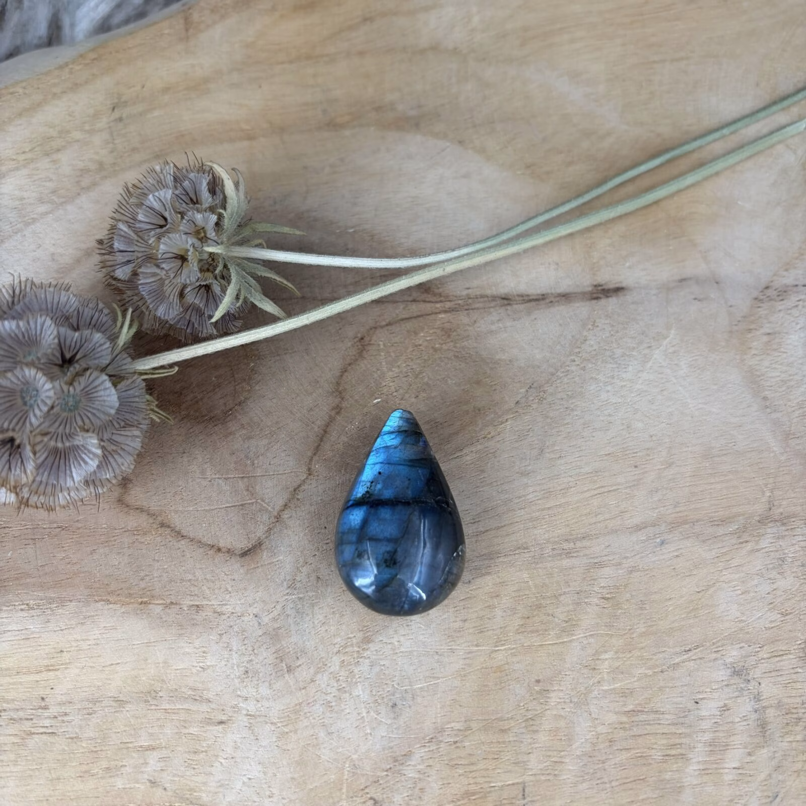 Een doorboorde Labradoriet hanger met blauwe glans op een rustieke houten ondergrond