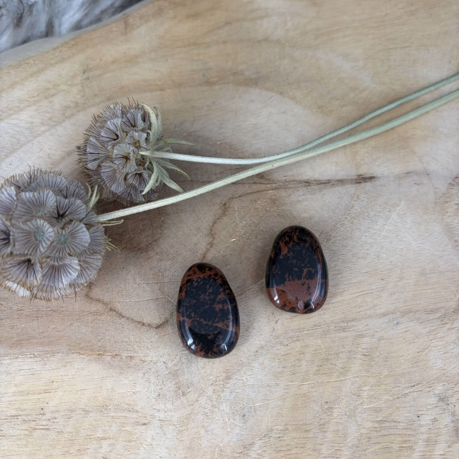 Een doorboorde Mahonie Obsidiaan hanger met roodbruine vlekken op een houten plank.